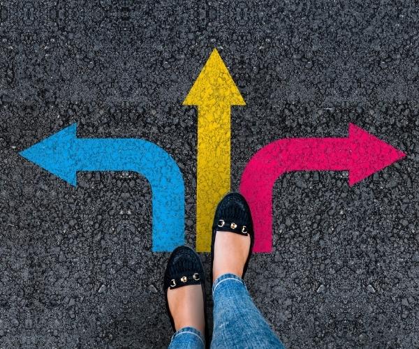 Person stands at a crossroads with arrows painted on the asphalt indicating directions left, straight, and right.