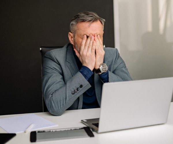 Frustrated real estate sales person covers his face while looking at spreadsheets